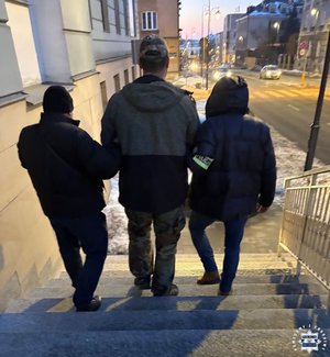 policjanci prowadzą zatrzymanego po schodach.