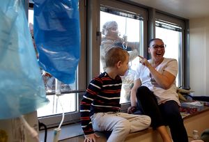 Dziecko, które siedzi w szpitalu na parapecie z kobieta machają do funkcjonariuszy BOA i alpinistów, którzy wiszą na linach poza oknem.