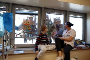 Dziecko, które siedzi w szpitalu na parapecie z kobieta machają do funkcjonariuszy BOA i alpinistów, którzy wiszą na linach poza oknem.