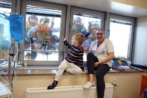 Dziecko, które siedzi w szpitalu na parapecie z kobieta machają do funkcjonariuszy BOA i alpinistów, którzy wiszą na linach poza oknem.