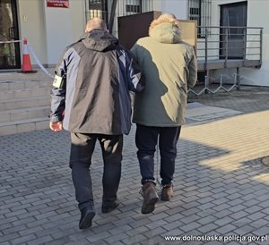 Policja, w kajdankach prowadzi zatrzymanego.