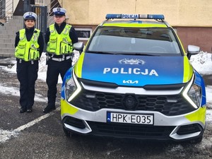 Dwoje umundurowanych policjantów przy radiowozie.
