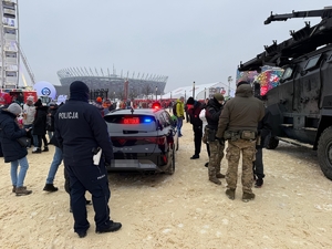 Policjant obok nieoznakowanego radiowozu wśród uczestników finału WOŚP na Błoniach Stadionu Narodowego.