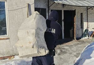 Policjant niesie na plecach drewno w worku.