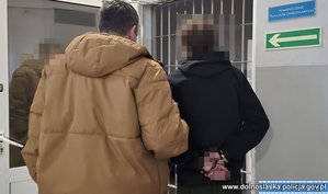 Nieumundurowany policjant prowadzi zatrzymanego mężczyznę.