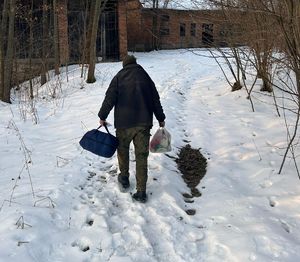 Na zdjęciu idący w śniegu mężczyzna. W rękach niesie reklamówkę z jedzeniem i śpiwór.