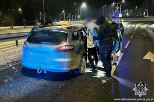 Policjanci z zatrzymanym przy samochodzie.
