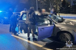 Policjanci z zatrzymanym przy samochodzie.