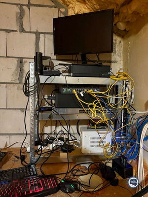 Zestaw komputerowy na metalowym stojaku, dwie klawiatury komputerowe i plątanina kabli.