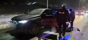 Policjant przy samochodzie i wokół zatrzymane osoby siedzące na ziemi.