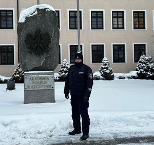 zima. budynek Akademii Policji w Szczytnie. policjant pozuje do zdjęcia.