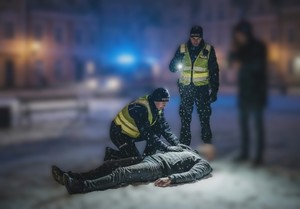 dwóch policjantów pomaga mężczyźnie leżącemu na ziemi.