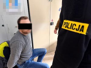 Zatrzymany mężczyzna siedzi na krześle podczas przesłuchania przez policjanta.