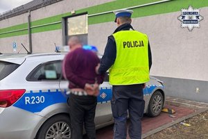 policjant prowadzi mężczyznę w kajdankach