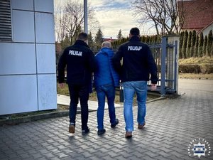 Dwaj funkcjonariusze prowadzą zatrzymanego.