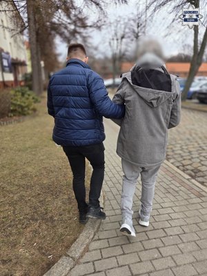 Policjant prowadzi chodnikiem zatrzymanego.