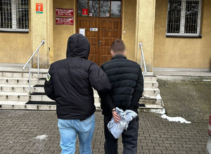 Policjant prowadzi zatrzymanego do budynku.