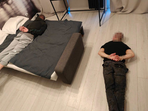 Zatrzymani mężczyzn - jeden leży na łóżku, drugi na podłodze. Obaj są skuci kajdankami.