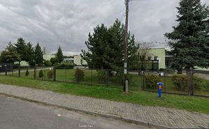 Budynek szkolny widziany przez płot i drzewa od strony ulicy.