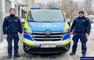 Dwaj policjanci stoja przy radiowozie.