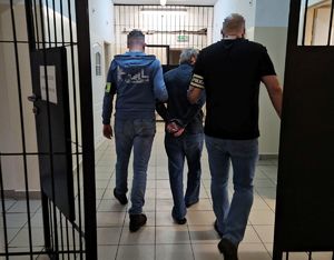 Policjanci prowadzą zatrzymanego do aresztu.