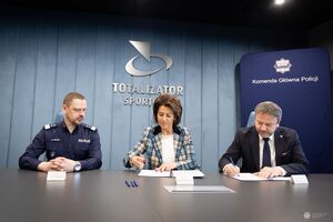 Komendant Główny Policji siedzi obok kobiety i mężczyzny z Totalizatora Sportowego. dwie osoby podpisują dokumenty.