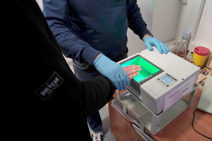 Mężczyzna przykłada palce do skanującego urządzenia.