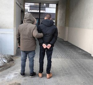 Funkcjonariusz trzyma zatrzymanego mężczyznę zakutego w kajdanki.