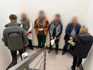 Funkcjonariusz i funkcjonariuszka Straży Granicznej oraz zatrzymane osoby stojące na klatce schodowej.
