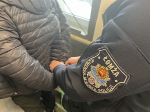 Policjant zakłada zatrzymanemu kajdanki.