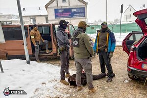 Policjanci z zatrzymanym, który skuty kajdankami lezy na ziemi.
