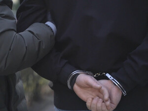 Mężczyzna zakuty w kajdanki prowadzony przez funkcjonariusza.