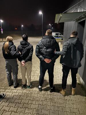 policjanci prowadzą zatrzymanych, stoją na parkingu.