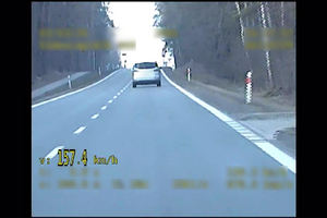 Widoczny samochód jadący przed radiowozem. W dolnym lewym rogu pojawia się żółty napis 157.4 km/h.