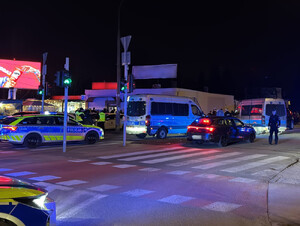 Trzy radiowozy policyjne stojące na ulicy. Obok policjant stojący obok samochodu osobowego zatrzymanego do kontroli.