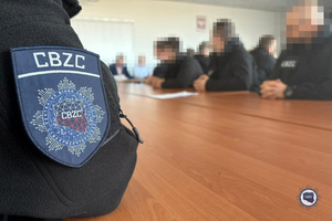Funkcjonariusze CBZC siedzą przy stole. Na pierwszym planie po lewej stronie naszywka z logo CBZC na bluzie funkcjonariusza.