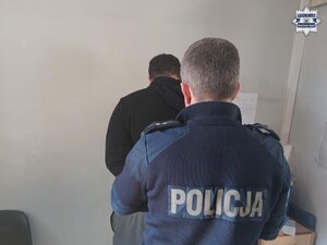 Mężczyzna skuty kajdankami, stoi przy ścianie.