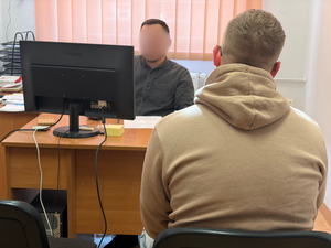 Policjant siedzący przy biurku przesłuchuje zatrzymanego mężczyznę siedzącego naprzeciwko niego.