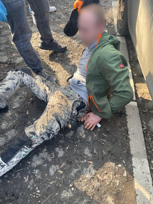 Zatrzymany mężczyzna zakuty w kajdanki siedzi na ziemi.