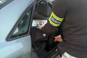 Policjant wyciąga z torby w samochodzie sztangę nielegalnych papierosów.