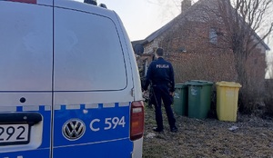 Oznakowany radiowóz stoi przed domem, a obok stoi policjant.