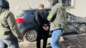 Dwaj policjanci z zatrzymanym przy samochodzie.