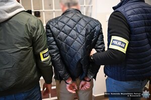 Dwaj funkcjonariusze prowadza zatrzymanego mężczyznę.