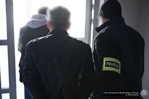 Dwaj funkcjonariusze prowadza zatrzymanego mężczyznę.