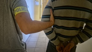 Mężczyzna w kajdankach prowadzony przez policjanta.