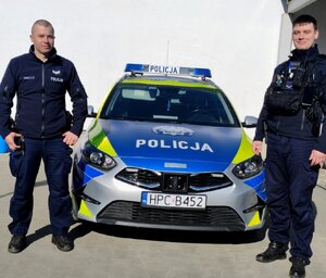 Dwaj policjanci stoją przy radiowozie.