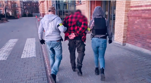 Policjanci prowadzą mężczyznę w kajdankach.