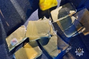 Noc. policjanci podczas kontroli drogowej przeszukują bagażnik. Żółte paczki.