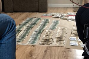 narkotyki porozkładane w samochodzie. Mężczyzna w kajdankach siedzi przy samochodzie. pieniądze rozłożone na stole.