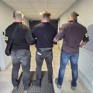 Dwaj policjanci prowadzą korytarzem zatrzymanego.
